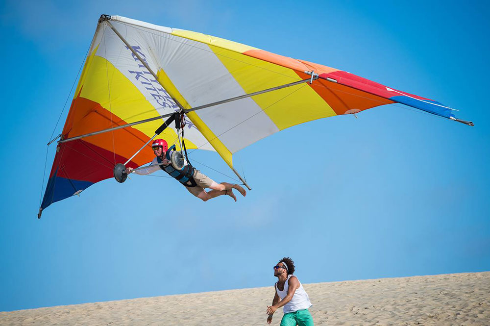A hang-gliding student flying above the dunes at Jockey’s Ridge with an instructor below